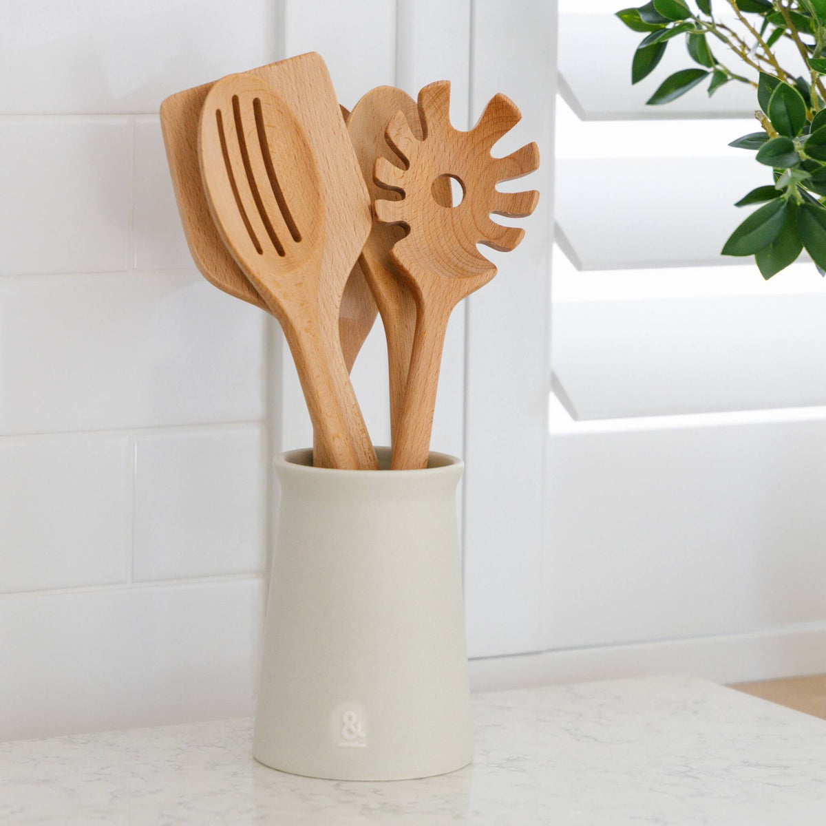 Beechwood utensils standing in a ceramic crock on a kitchen bench