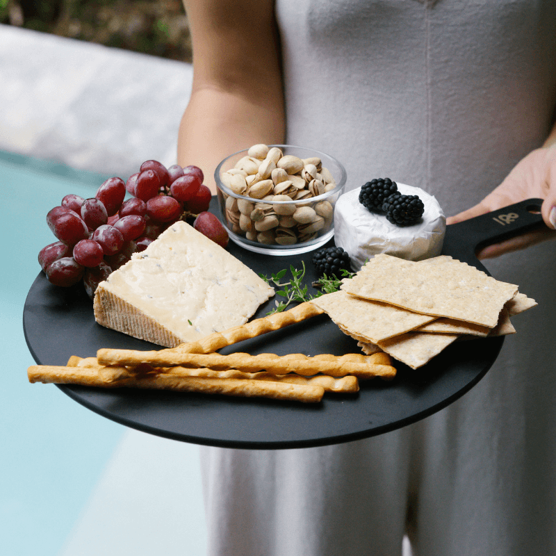A glass dip bowl of nuts on a cheese board with grapes and crackers