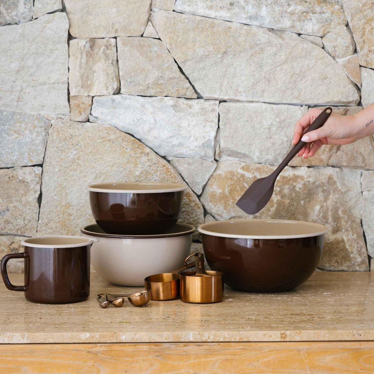 Macadamia enamel bowls stacked on a timber bench against a stone wall