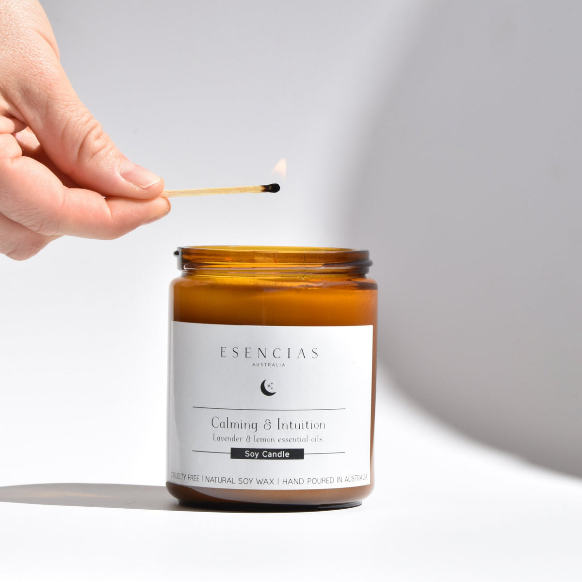 Esencias Calming & Intuition soy candle in amber glass, being lit with a match
