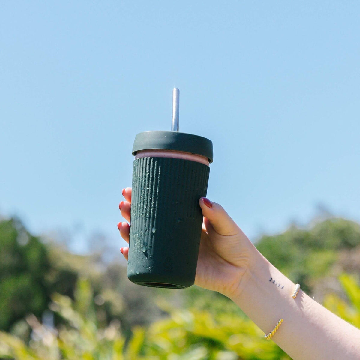 Holding the Moss smoothie cup with its glass straw outdoors