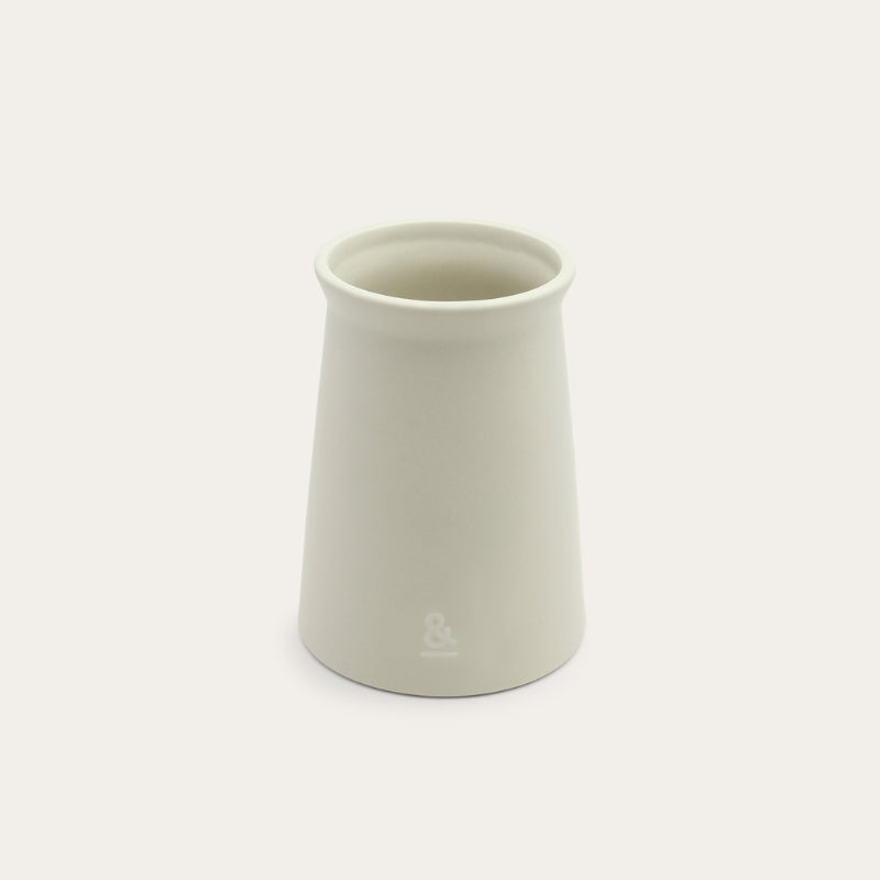 The ceramic utensil holder empty, showing its tapered shape and embossed logo