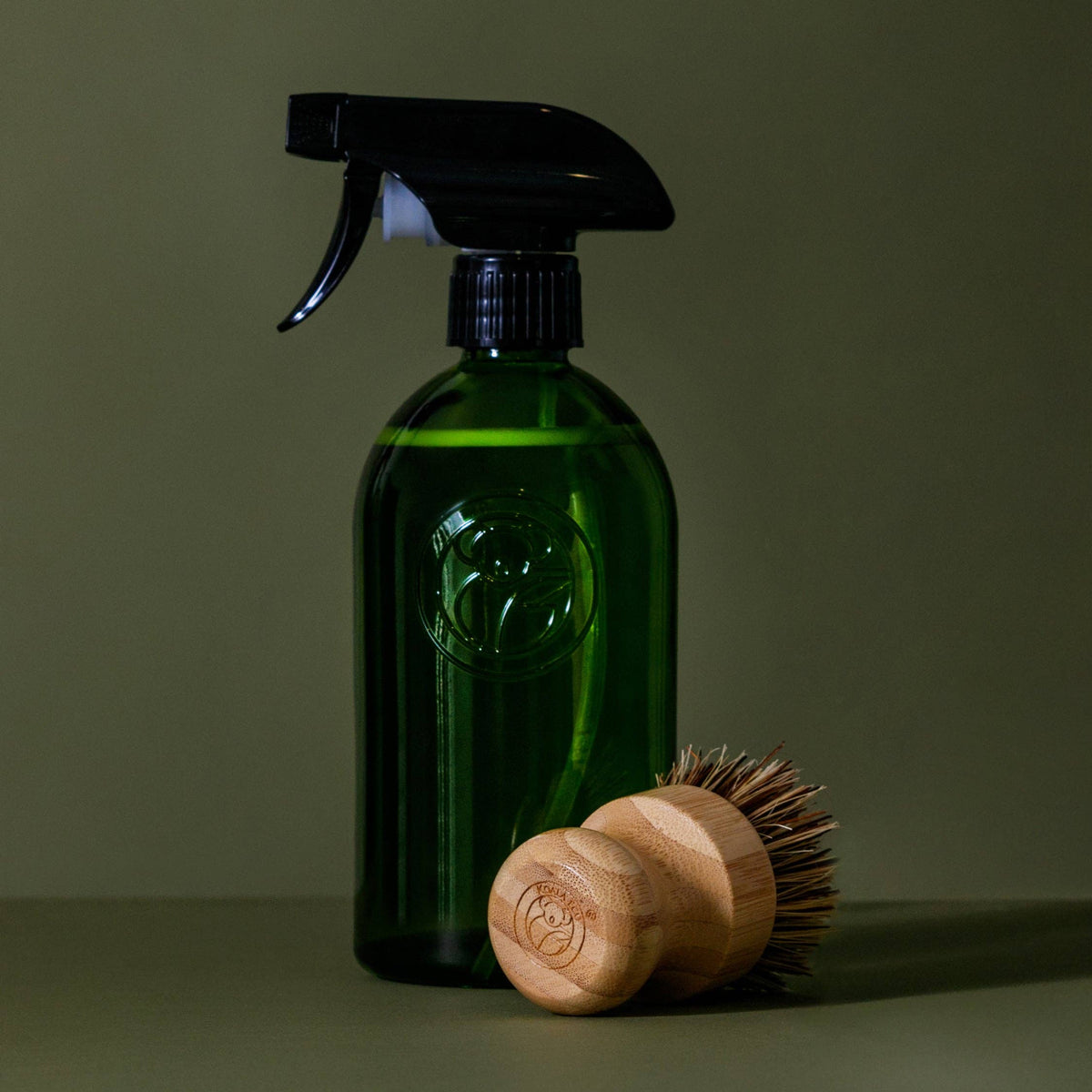 Koala Eco bamboo and agave scrubbing brush resting beside a green glass Koala Eco spray bottle