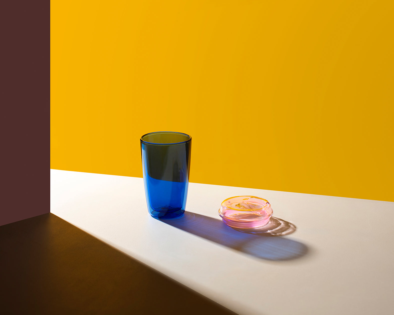 Blue glass and pink rubber band on a white surface with a yellow and brown background