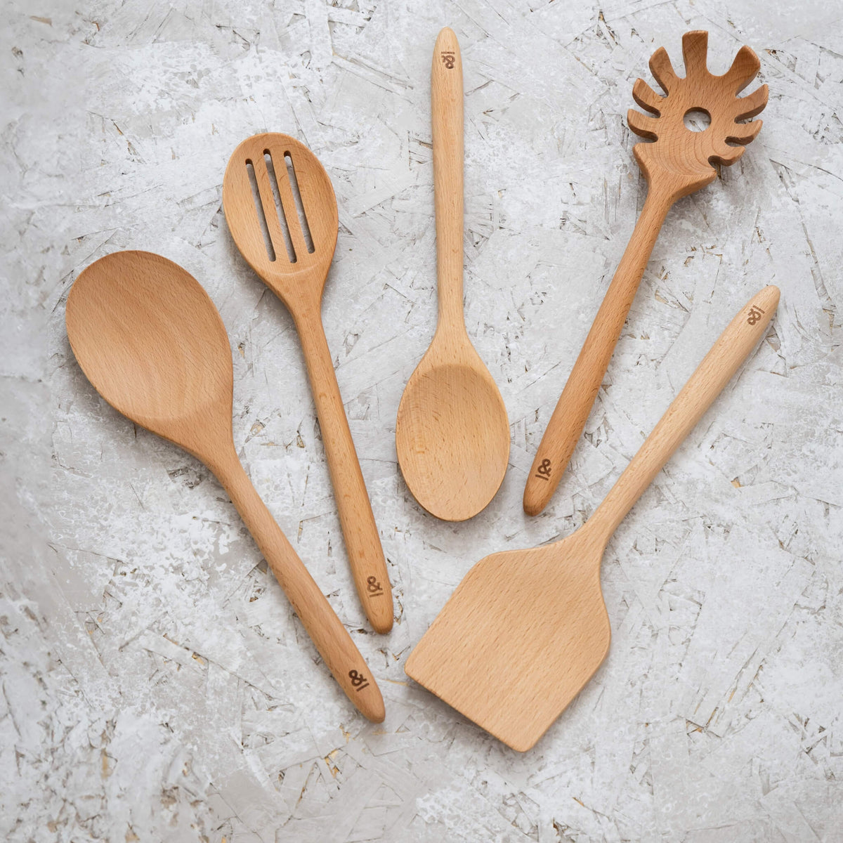 All five beechwood utensils laid out, spoon, slotted spoon, large serving spoon, spaghetti spoon and turner