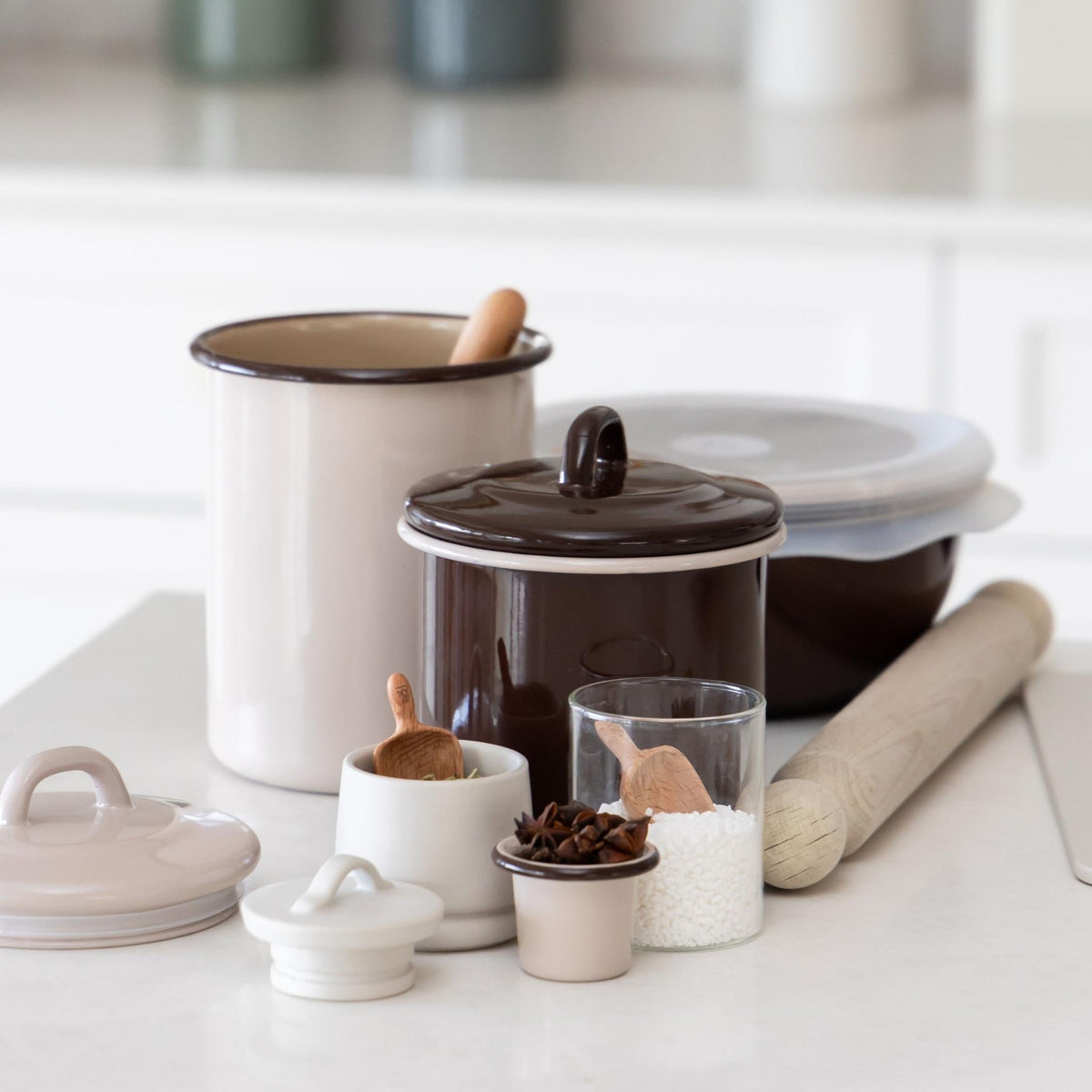 Macadamia enamel storage jars on a baking bench with a wooden scoop, spices and a rolling pin