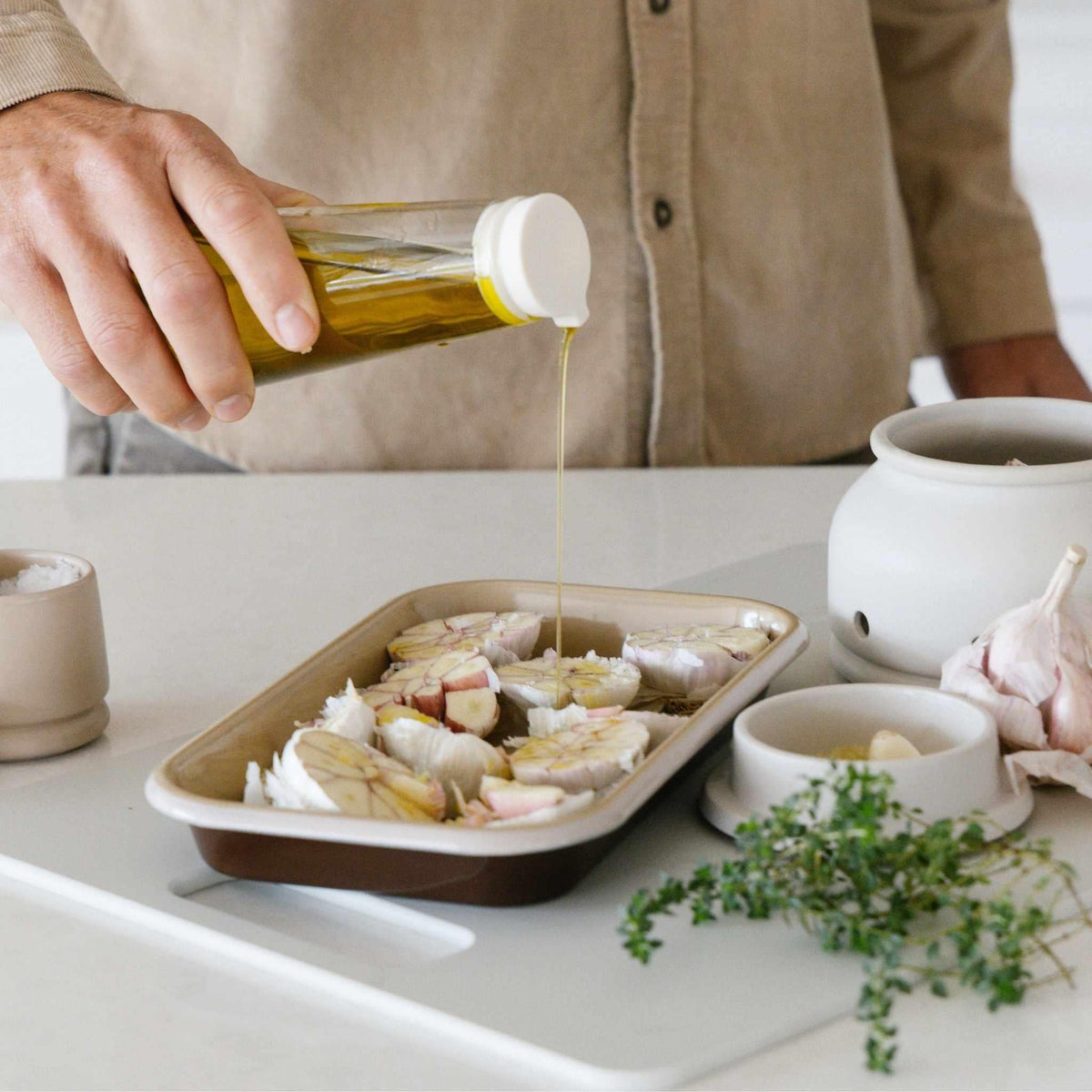 Olive oil being poured over fish in a Macadamia enamel baking tray