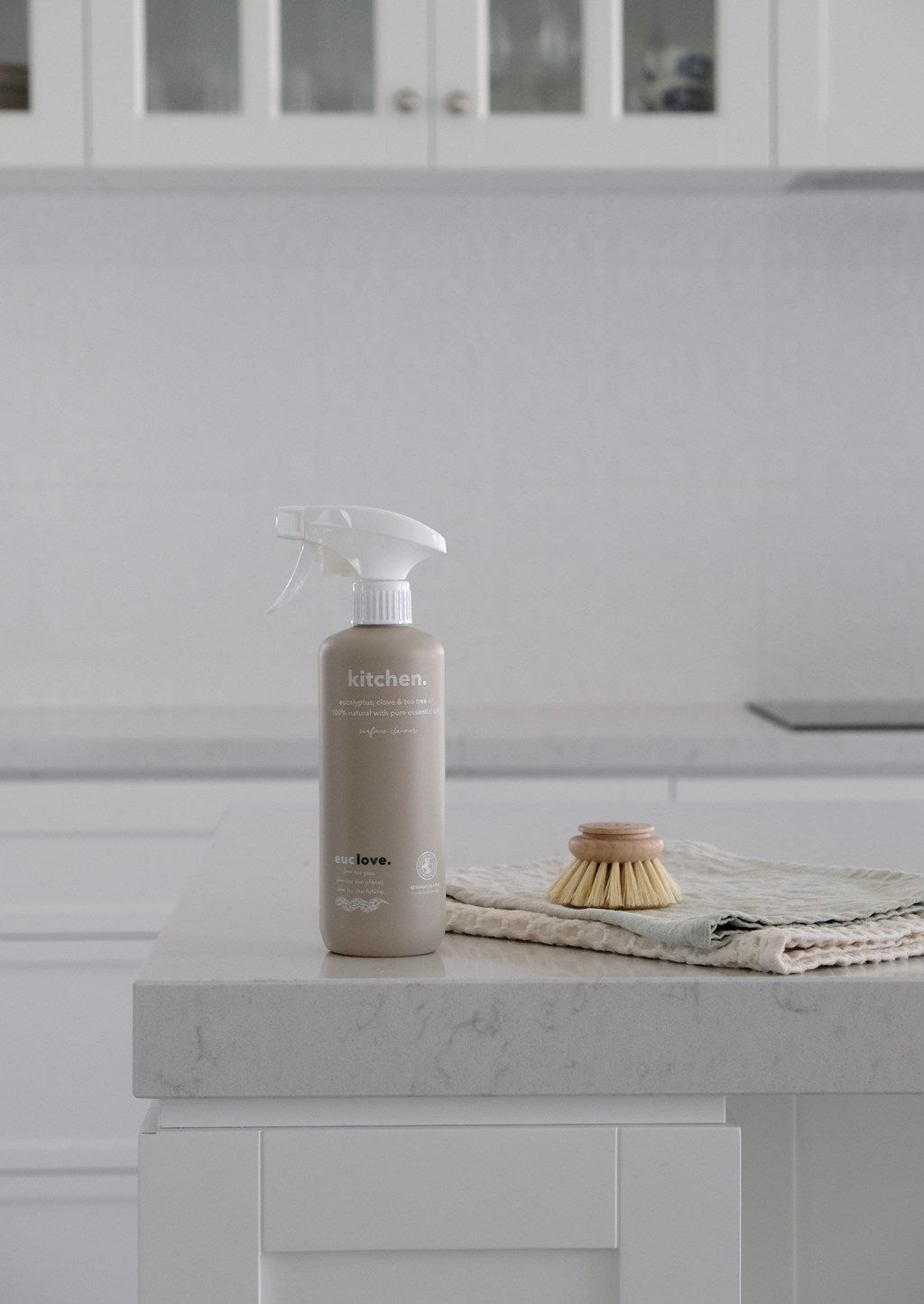 Euclove kitchen cleaner spray bottle on a marble benchtop beside a wooden dish brush and linen cloth