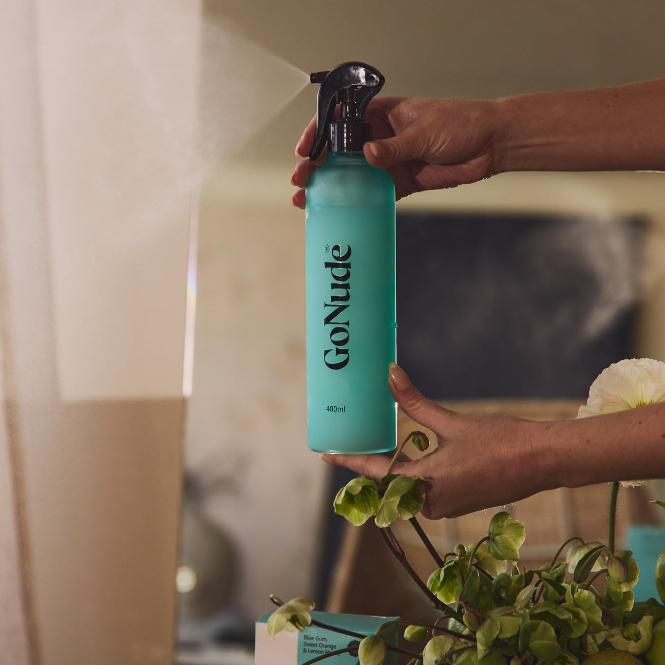 Go Nude glass and mirror cleaner sprayed from a turquoise 400ml refillable bottle, with the Blue Gum, Sweet Orange and Lemon Myrtle carton behind