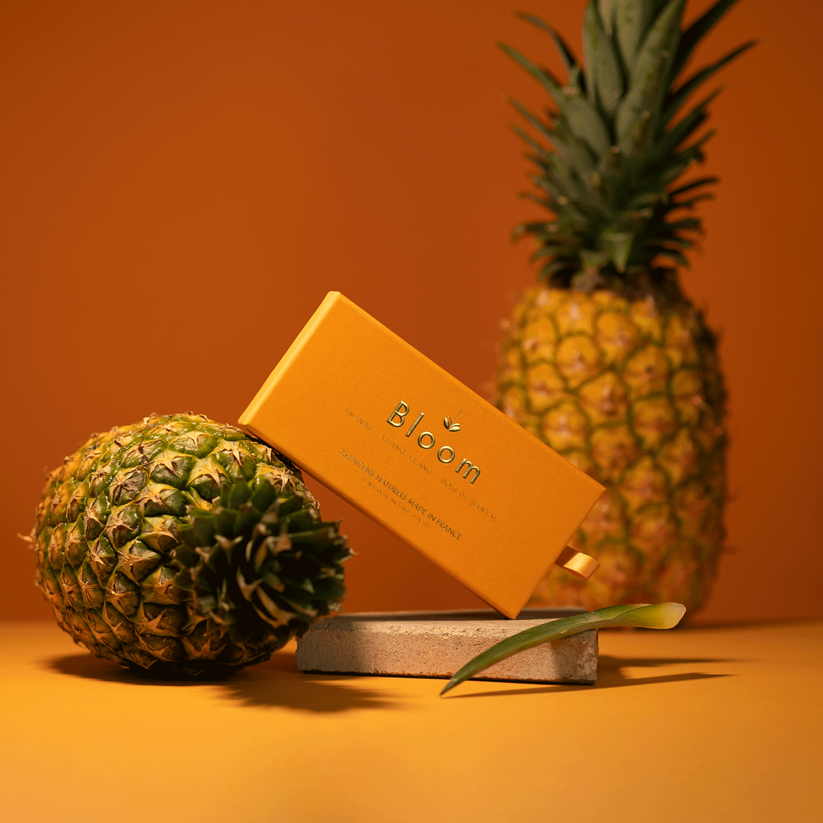 Bloom France Pineapple incense box styled with fresh pineapples on a warm amber backdrop