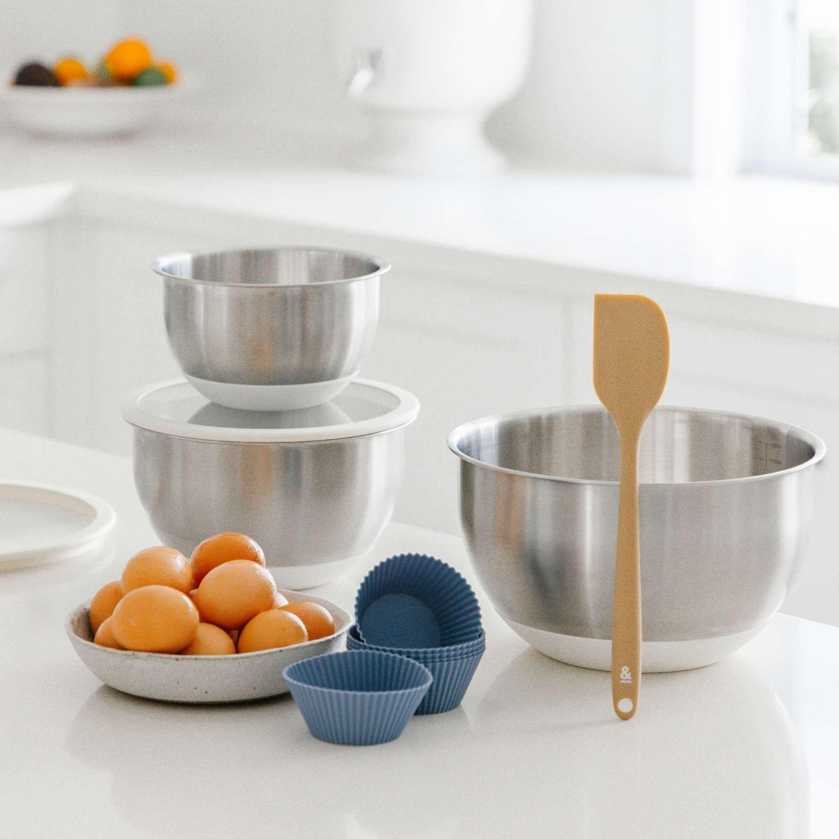 Blueberry silicone muffin cups on a kitchen bench with stainless mixing bowls and eggs