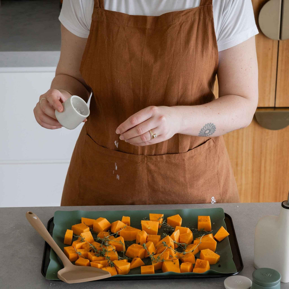 Seasoning a tray of roast pumpkin by hand from a ceramic pod