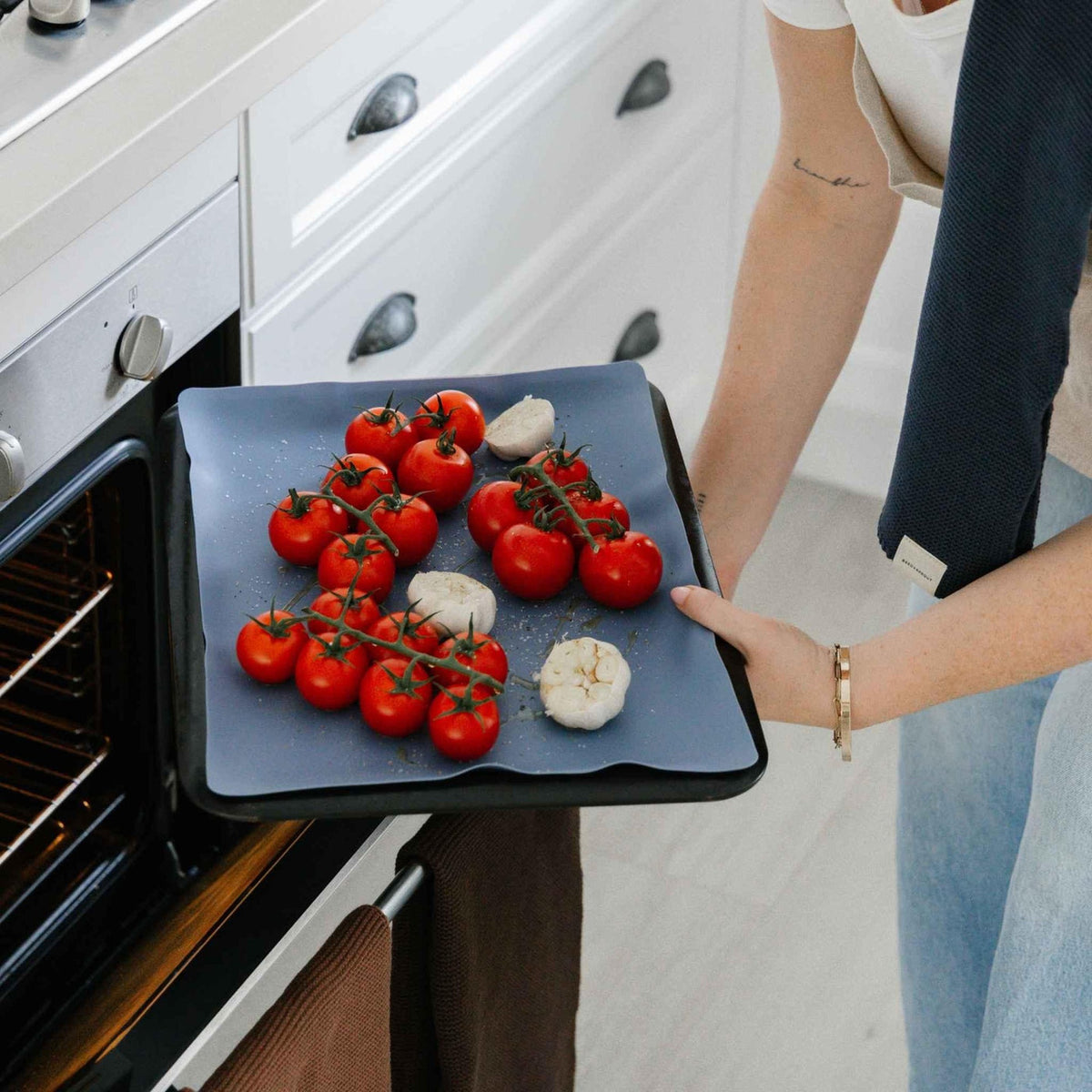 Blueberry silicone baking mat on a tray of tomatoes and garlic, going into the oven