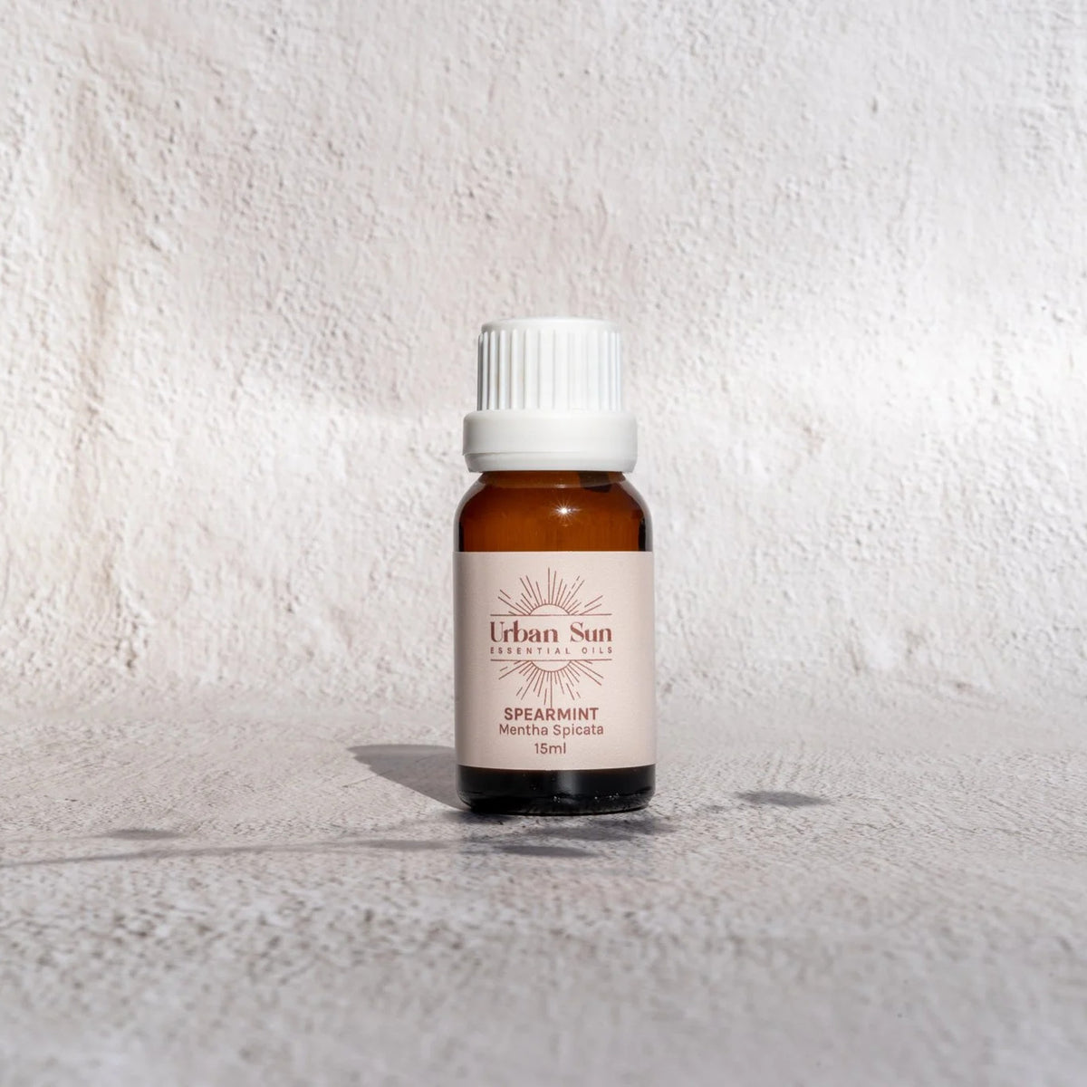 Urban Sun Spearmint essential oil 15ml, amber glass bottle on a textured wall