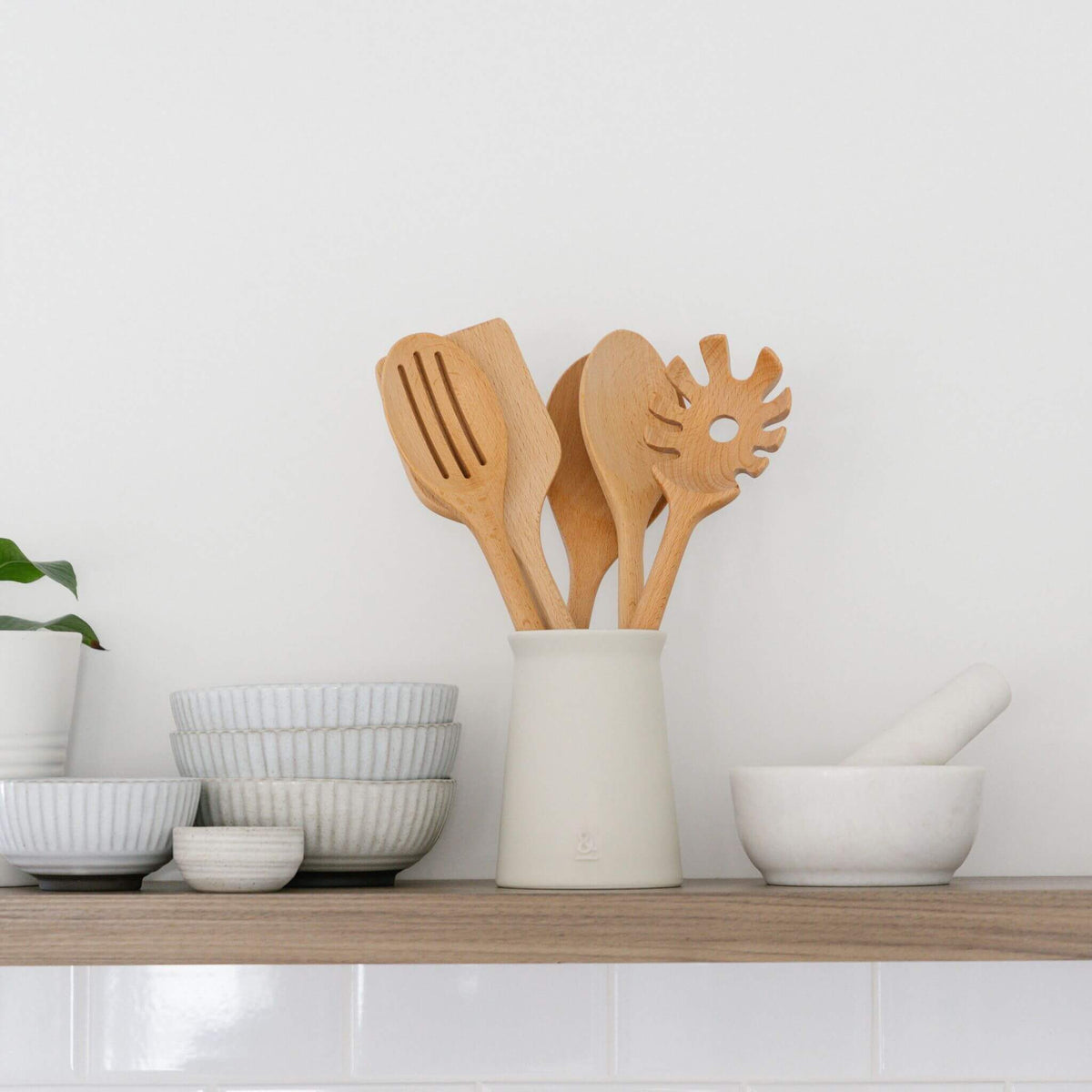 Ceramic utensil holder on a timber bench beside stacked bowls and a mortar and pestle