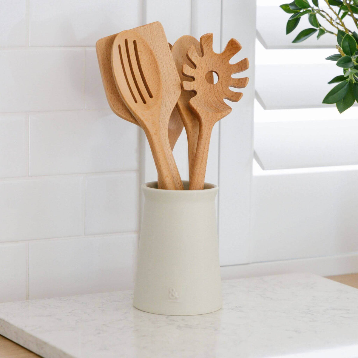 Wooden utensils standing upright in the ceramic holder on a stone benchtop