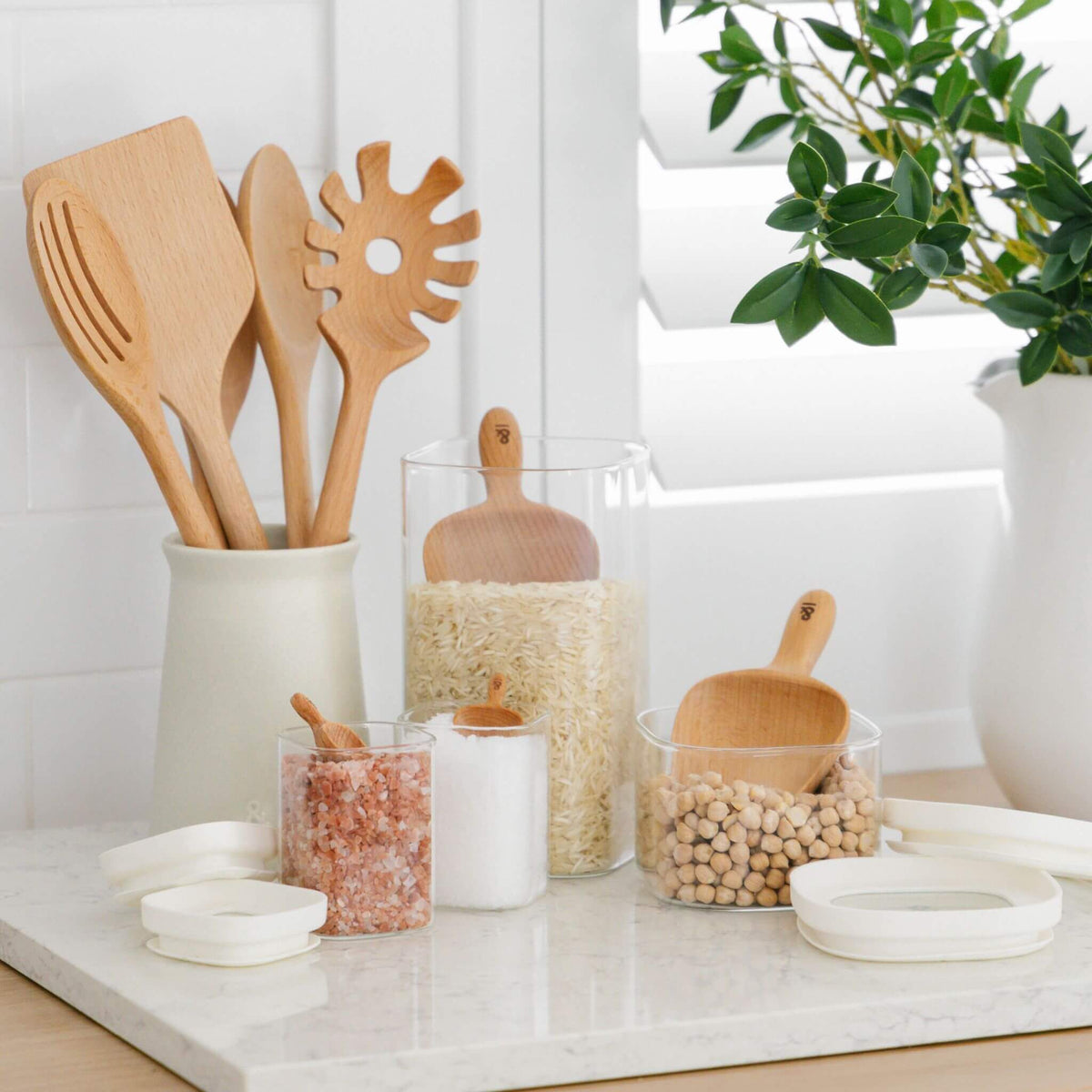 Ceramic utensil holder in a kitchen corner with glass pantry jars and a wooden scoop